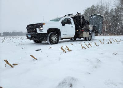 White pickup carrying a portapotty through the snow