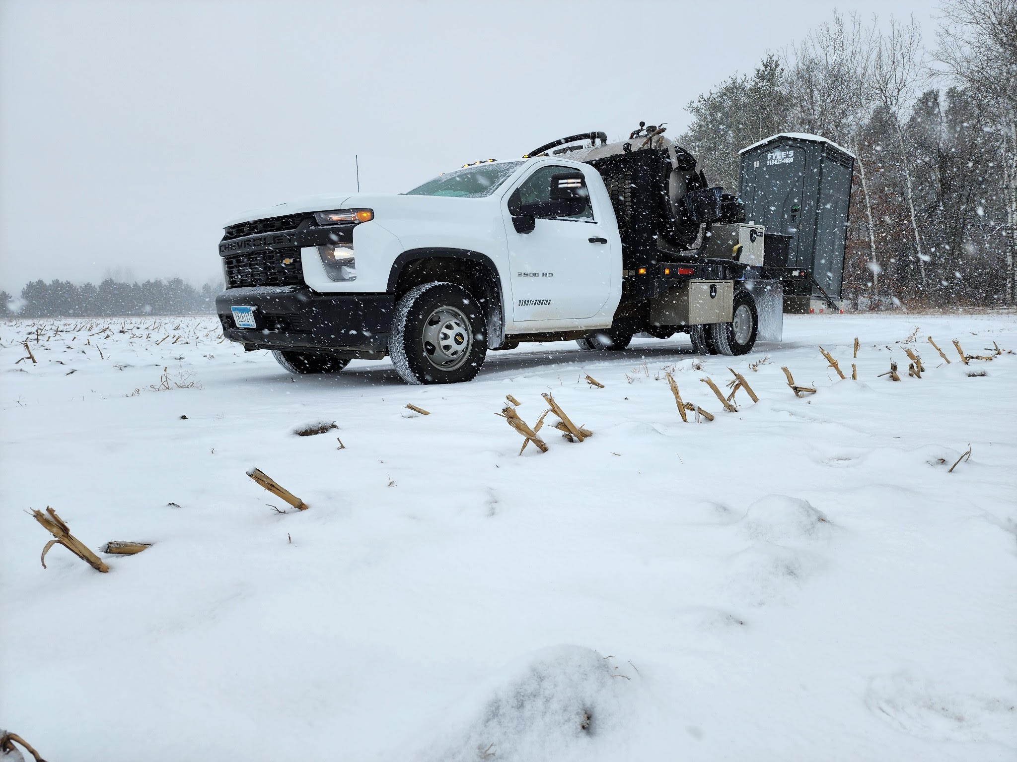 White pickup carrying a portapotty through the snow
